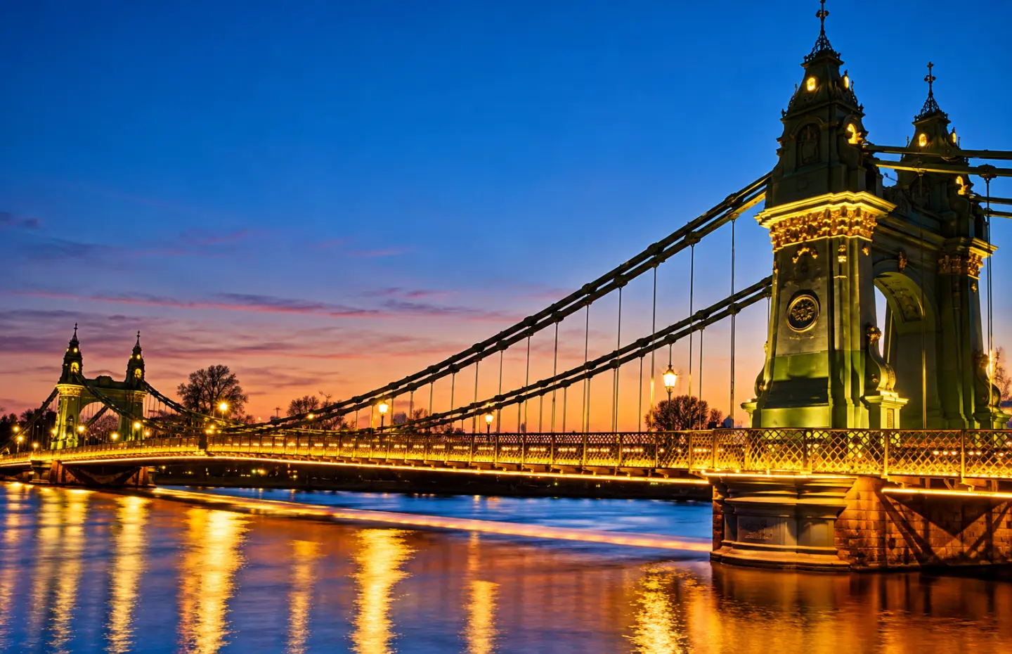 Hammersmith Bridge lit up at dusk, reflected in the River Thames