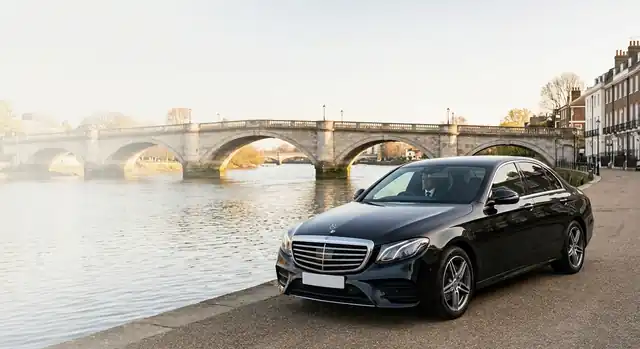 Black Mercedes saloon parked beside the River Thames in Richmond, with Richmond Bridge behind